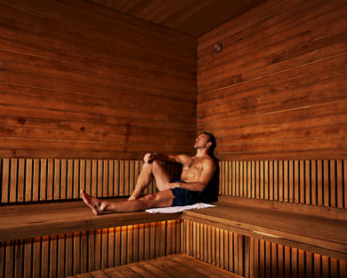 Man sitting in a sauna with his legs out and leaning against the wall with his eyes closed.