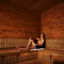 Man sitting in a sauna with his legs out and leaning against the wall with his eyes closed.