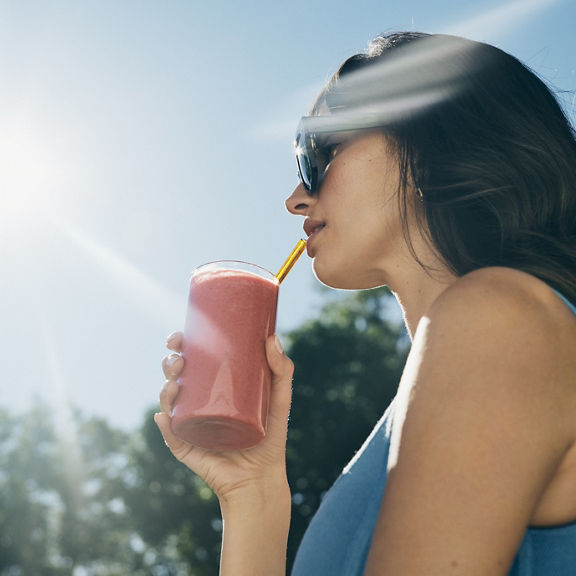 An attractive female wearing oversized sunglasses on a sunny day drinking a pink-colored smoothie