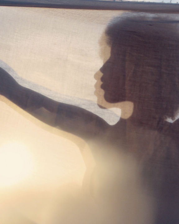 Silhouette of woman with afro hair behind curtain in sunset on the beach. Blurred portrait, profile view.