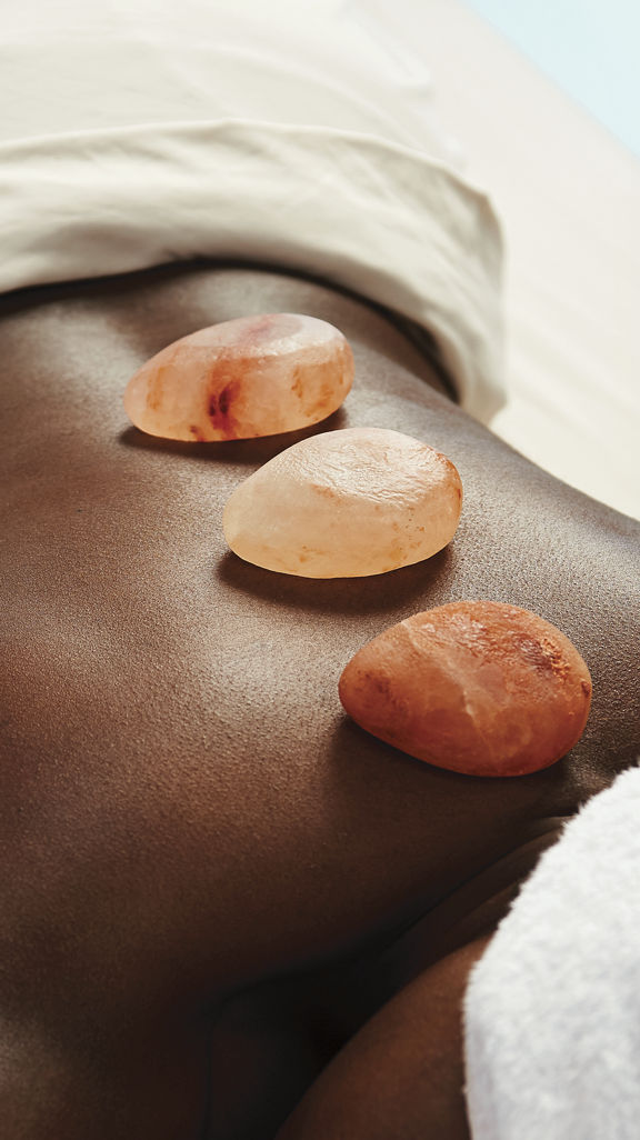 A woman lying on a massage table with hot stones on her back and her head wrapped in a white towel