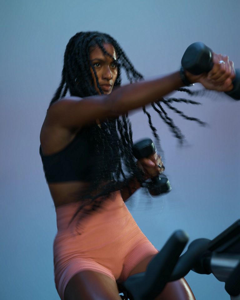 Cyclist actively using a dumbbells during an AMP spin class at Life Time