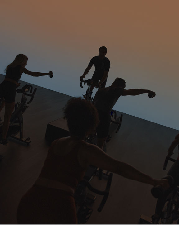 EDG spin class riding in silhouette, riders with their right arms extended holding a weight