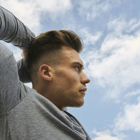 A young man exercising outside and stretching his arm over his head