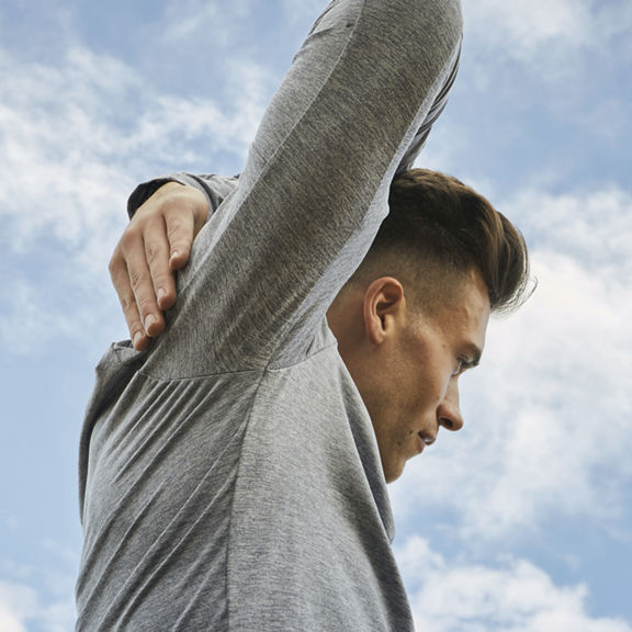 A young man exercising outside and stretching his arm over his head