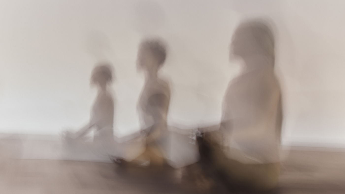 Close up stylized blurred image of three people in meditation at a surrender yoga class