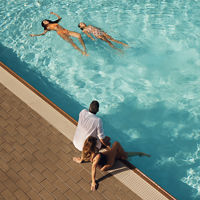 Mother and father sitting on the edge of an outdoor pool watching their children swim