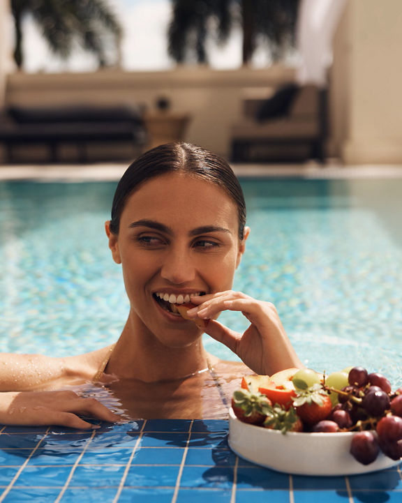 An attractive adult female coming out of the pool to enjoy a bowl of fresh fruit
