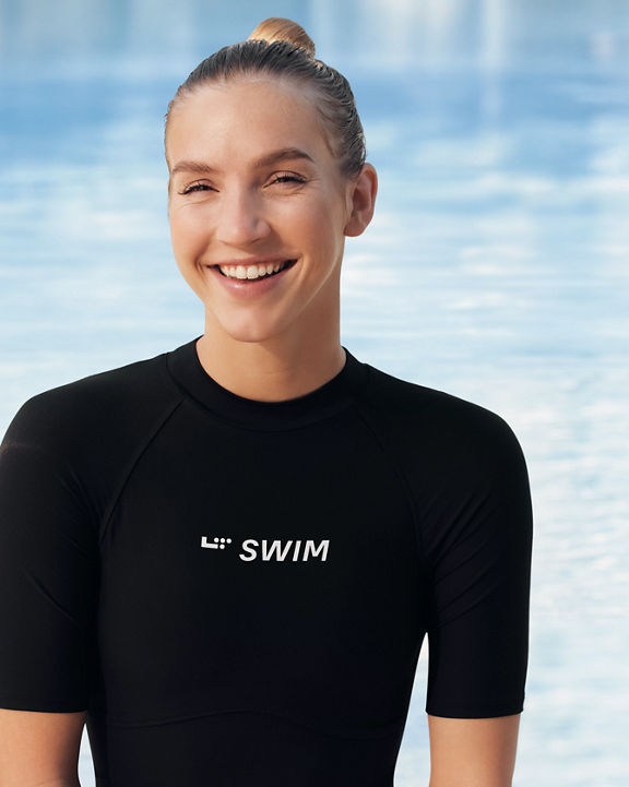 girl in a black L T swim shirt smiling by a pool