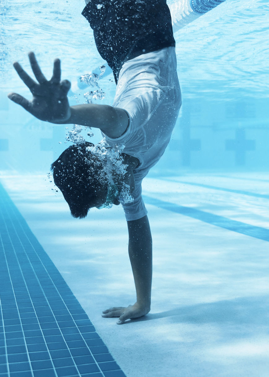 a boy standing on one hand under water