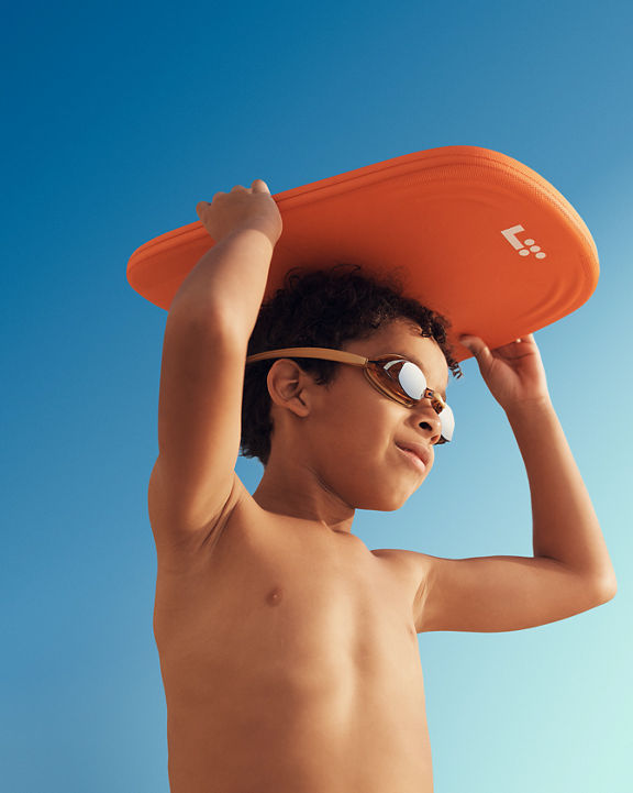 boy wearing swim goggles holding an orange kick board