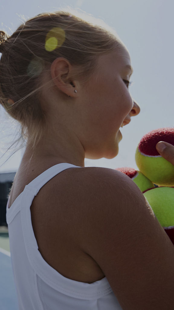 Close view of a female child holding tennis balls on an outdoor tennis court
