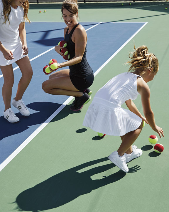A group of children playing tennis on an outdoor tennis court