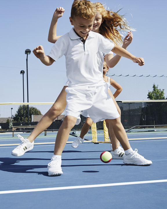 A group of children playing on an outdoor tennis court