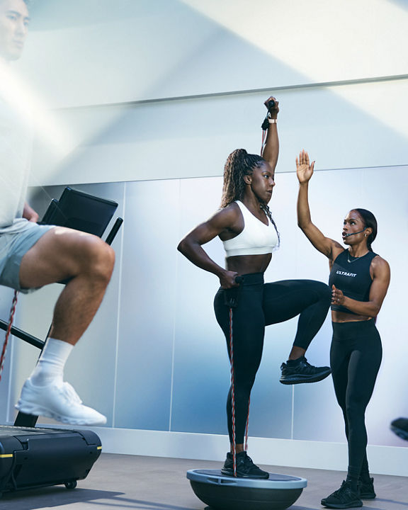 Person balancing on a bosu ball on one foot being guided by an UltraFit instructor