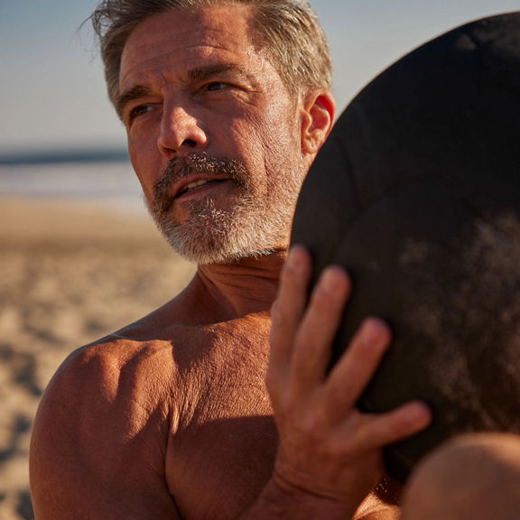 an older man works out with a medicine ball on the beach