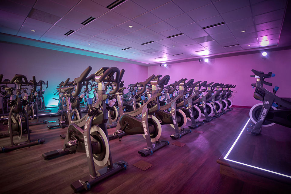a purple lit cycling studio with rows of stationary bikes