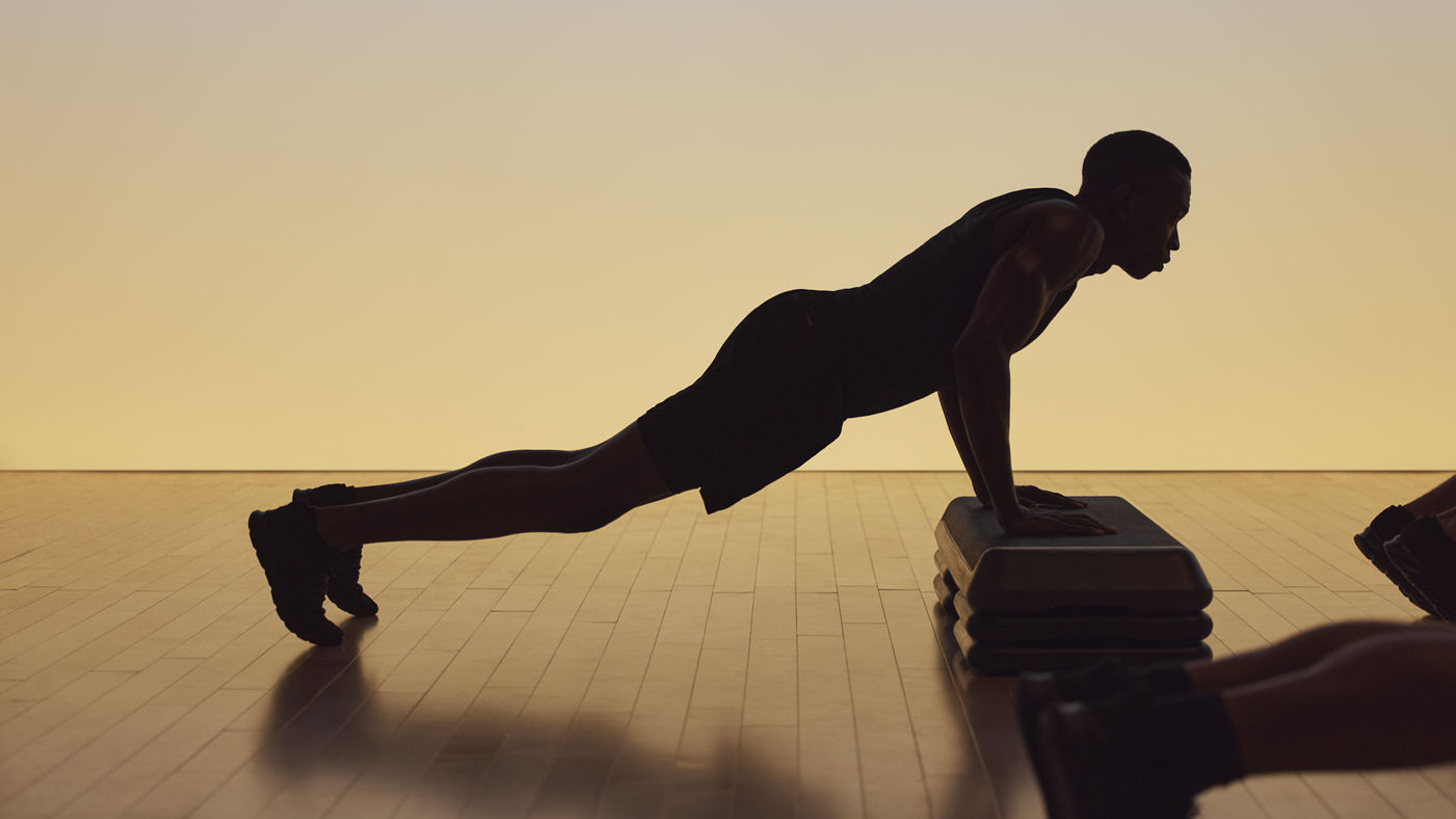 Xtreme cardio class member in elevated plank on a step bench at Life Time