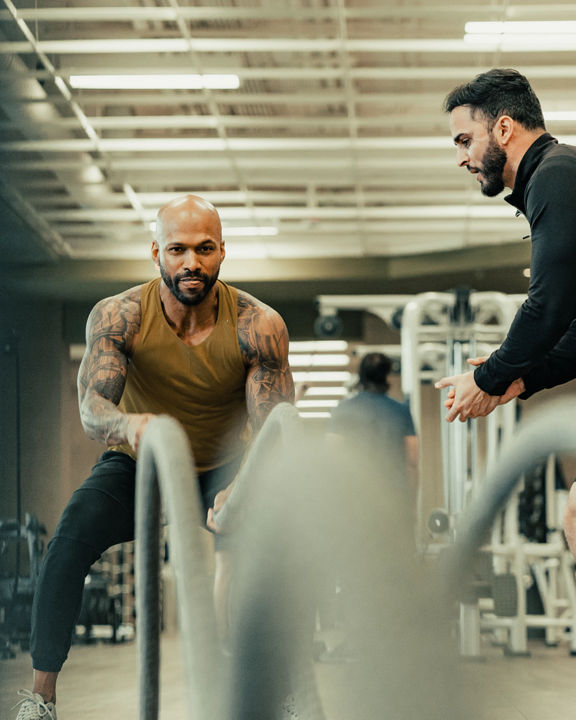 A male trainer training a male client with battle ropes.