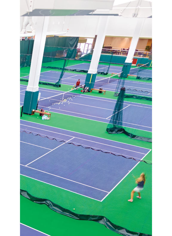 A row of five indoor tennis courts surrounded by green curtains