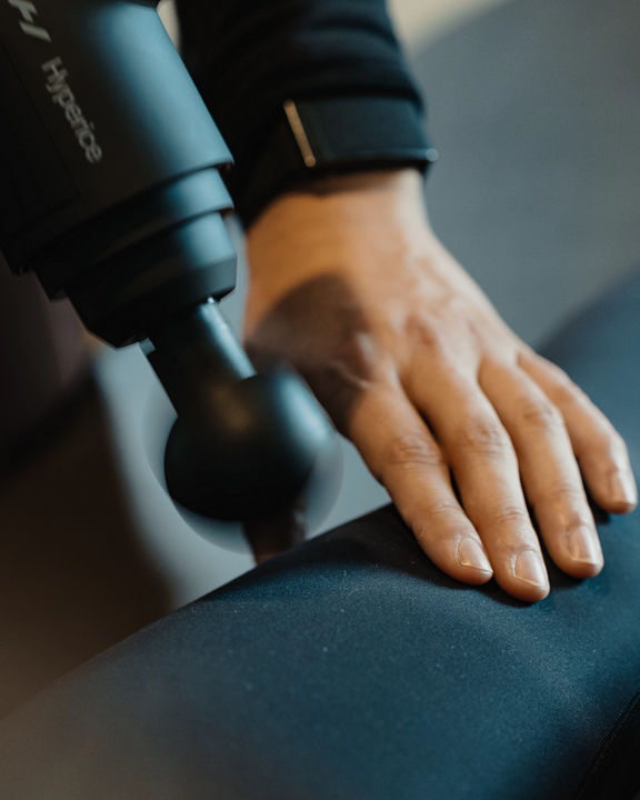 A Life Time personal training using a Hyperice massager on a member's leg during a dynamic stretch session