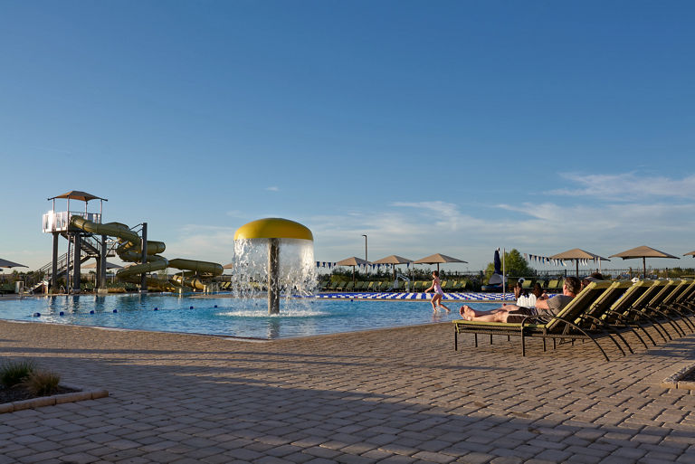 a young girl runs into an outdoor pool complete with mushroom waterfall, lap pool, waterslides, and surrounded by lounge chairs