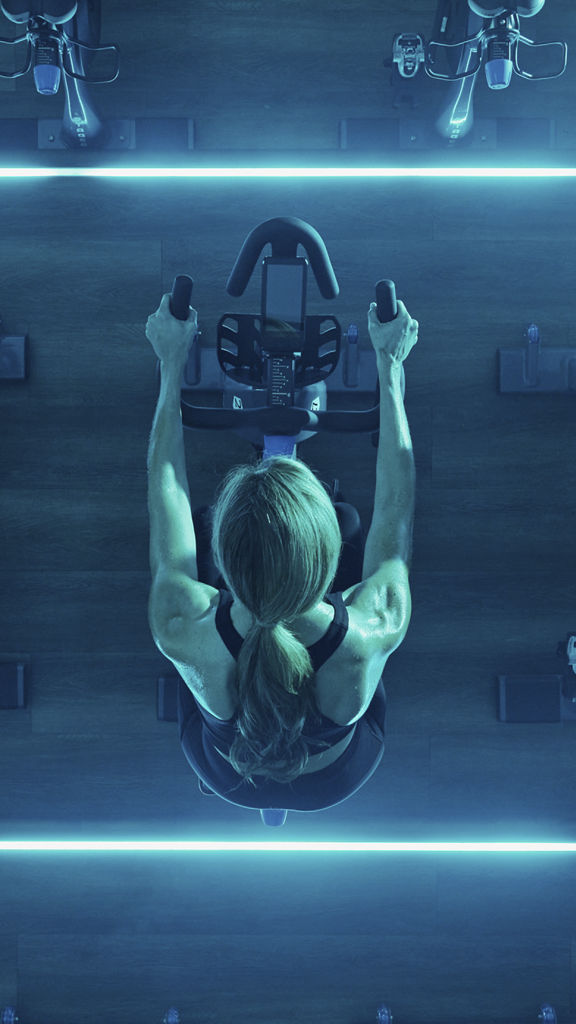 Overhead view of a female sitting on a stationary bike in a blue-lit cycle studio