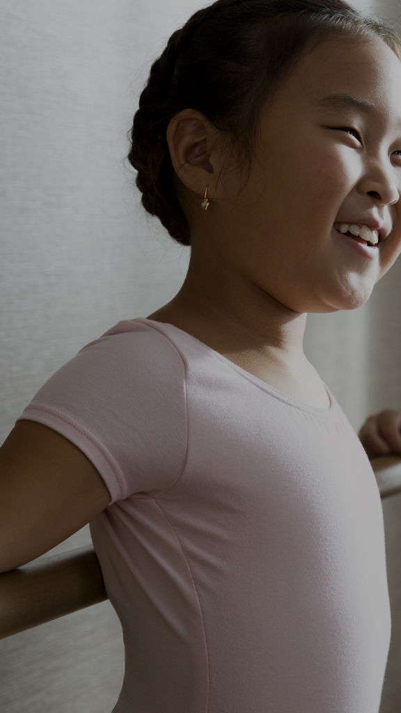 Two young girls in pink leotards smiling while standing in a studio next to a dance bar