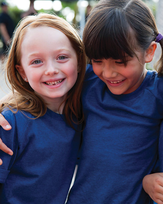 Close view of three female children wearing blue T-shirts huddled together with their arms around each other