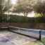 An outdoor pickleball court surrounded by a stone wall and tall trees