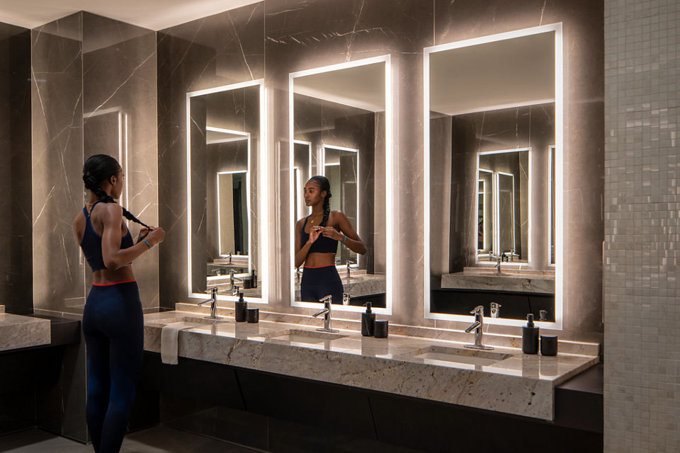 A female braiding her hair while looking into a mirror in the Life Time One Wall locker room