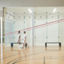 Two men walking by an open squash court at the Life Time South Austin club location