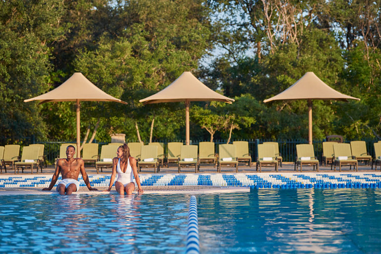 A man and woman smiling at each other while sitting poolside with their feet in the water