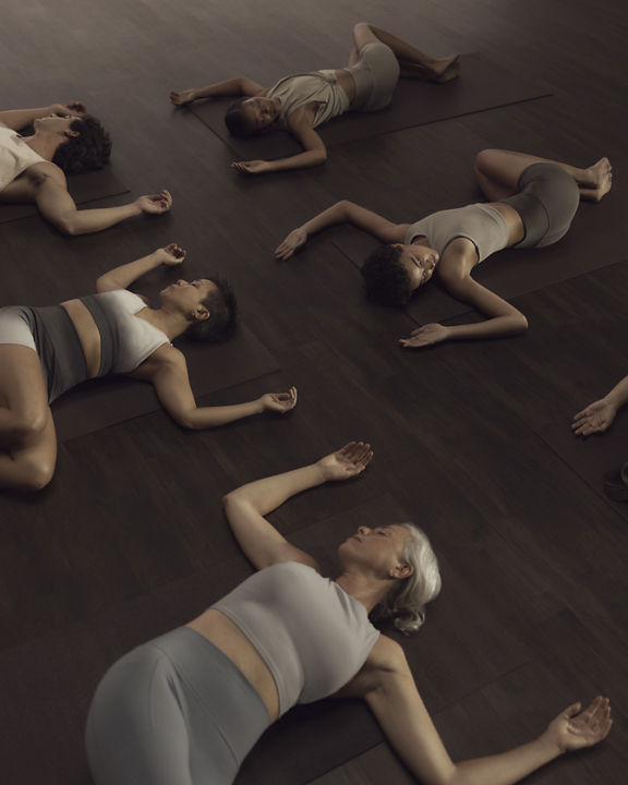 Surrender yoga class stretch with people on their back, hips twisted and arms in goal post position