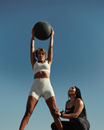A Life Time Dynamic Personal Trainer providing support while a participant holds a medicine ball up over her head