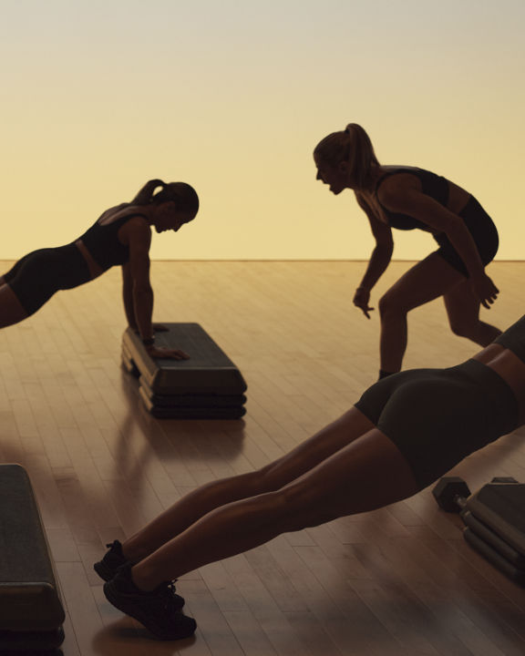 Xtreme cardio class members in elevated plank being encouraged by a Life Time instructor